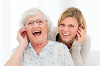 A senior and caregiver share headphones while enjoying a song together A senior and caregiver share headphones while enjoying a song together